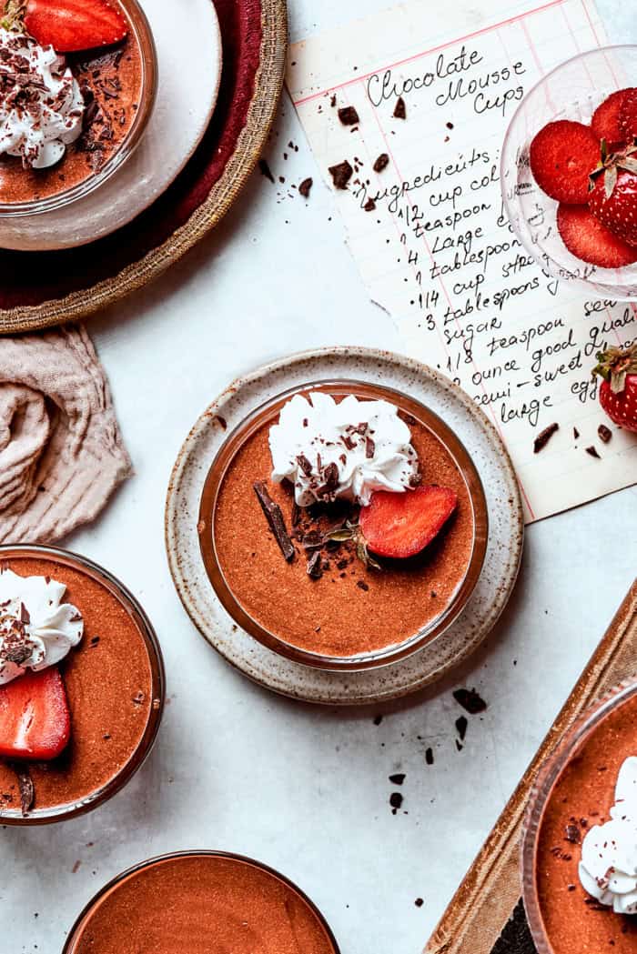 These decadent and delicious Chocolate Mousse Cups are the perfect personal-sized dessert! Serve them at a party and they’ll disappear FAST. overhead photo of chilled chocolate mousse cups garnished with whipped cream and strawberries