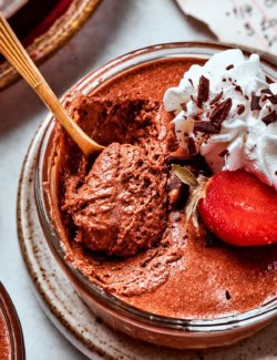 close-up photo of a cup of chocolate mousse with whipped cream and strawberries, with a spoon digging in