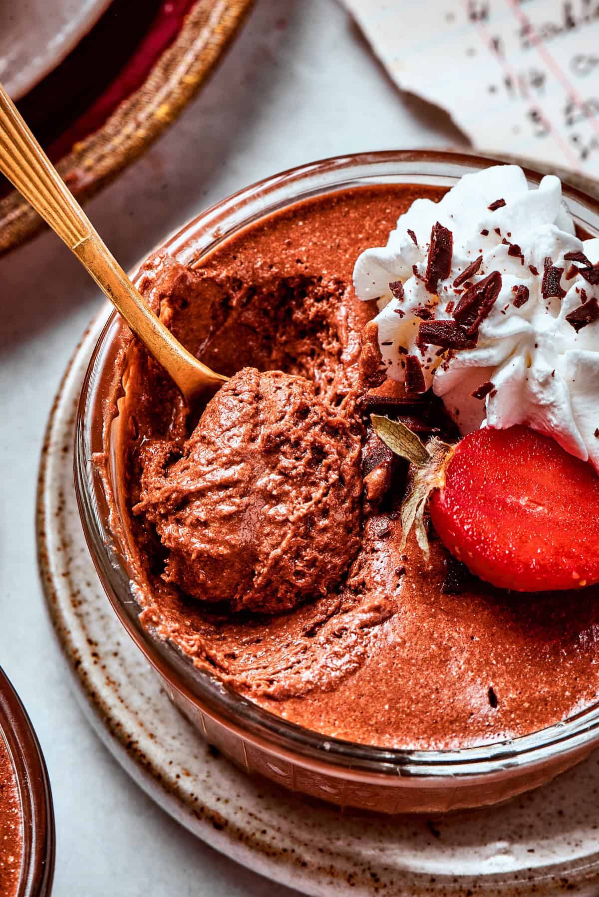These decadent and delicious Chocolate Mousse Cups are the perfect personal-sized dessert! Serve them at a party and they’ll disappear FAST. close-up photo of a cup of chocolate mousse with whipped cream and strawberries, with a spoon digging in