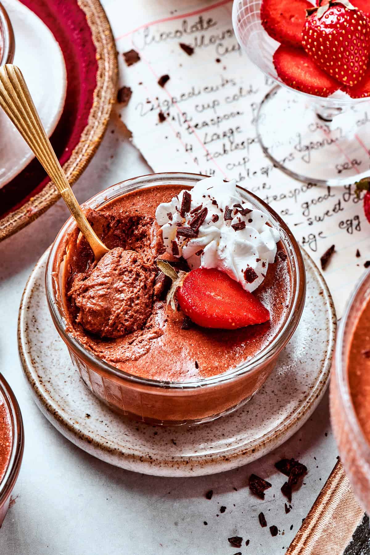 These decadent and delicious Chocolate Mousse Cups are the perfect personal-sized dessert! Serve them at a party and they’ll disappear FAST. a cup of chocolate mousse with whipped cream and strawberries
