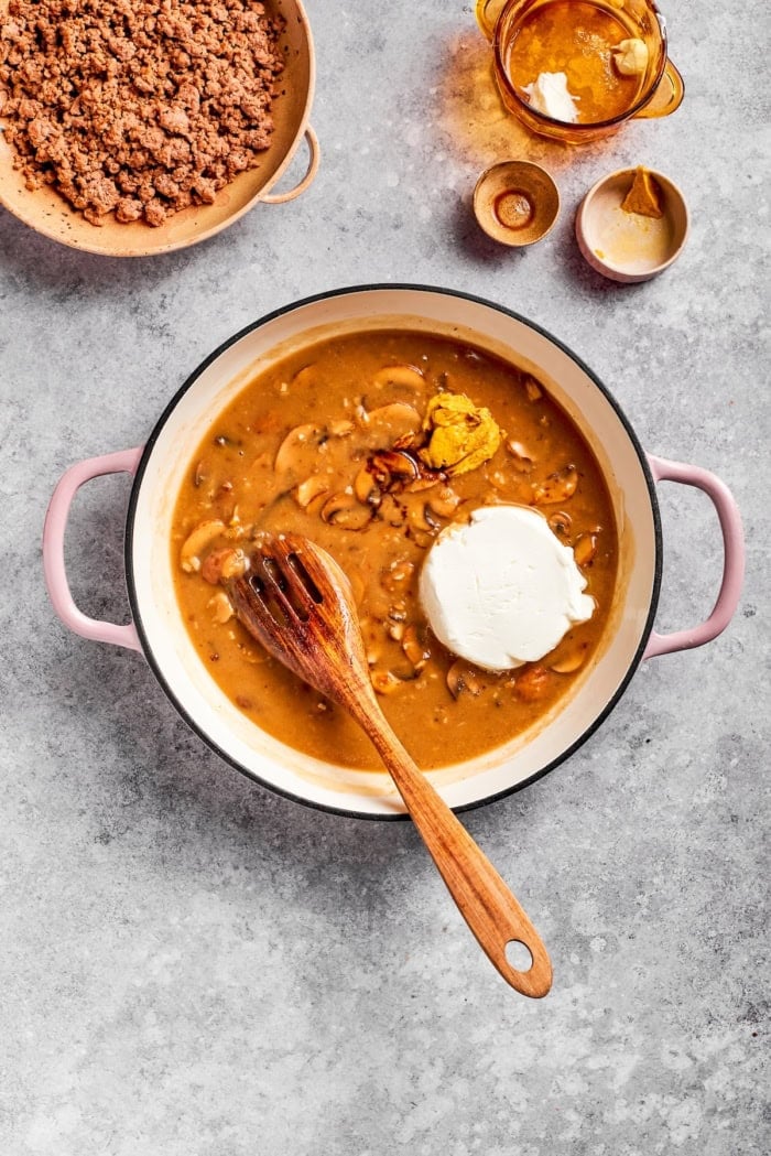 This creamy Ground Beef Stroganoff recipe is made from scratch without canned soup! An easy, budget-friendly dinner your family will love. Sour cream and mustard added to pan of ground beef stroganoff sauce.