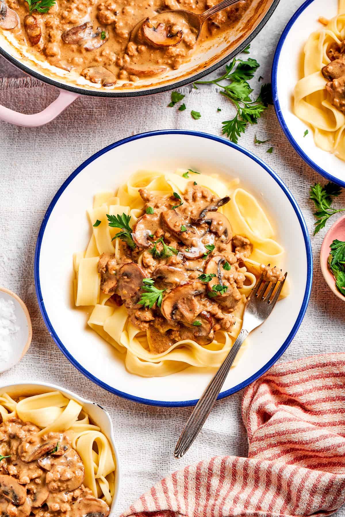 This creamy Ground Beef Stroganoff recipe is made from scratch without canned soup! An easy, budget-friendly dinner your family will love. ground beef stroganoff on a white plate with a blue rim
