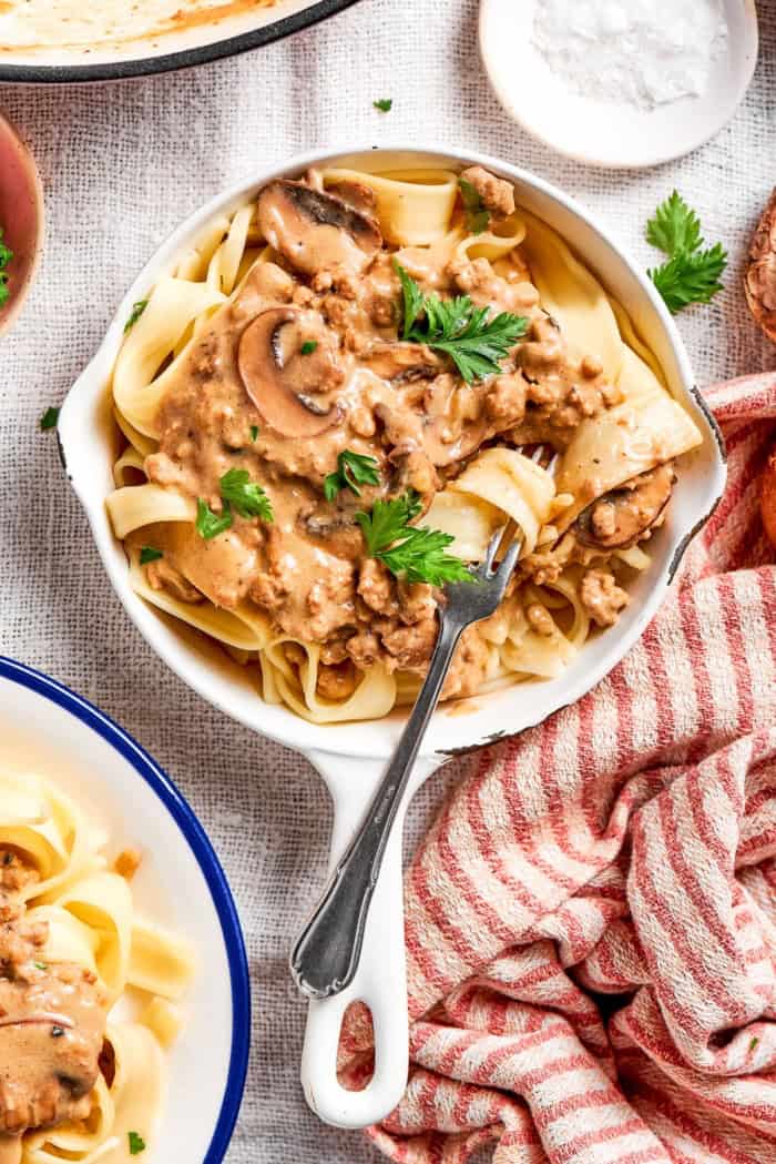 This creamy Ground Beef Stroganoff recipe is made from scratch without canned soup! An easy, budget-friendly dinner your family will love. Noodle twirled around fork in skillet of ground beef stroganoff.