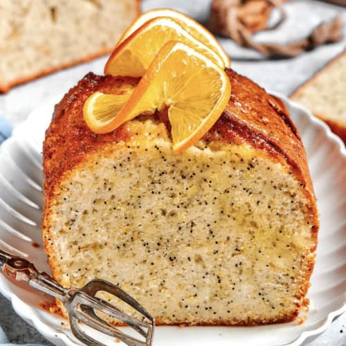 a loaf of orange poppy seed bread, sliced through the center, with fresh oranges slices on top