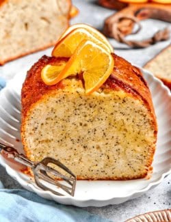 a loaf of orange poppy seed bread, sliced through the center, with fresh oranges slices on top