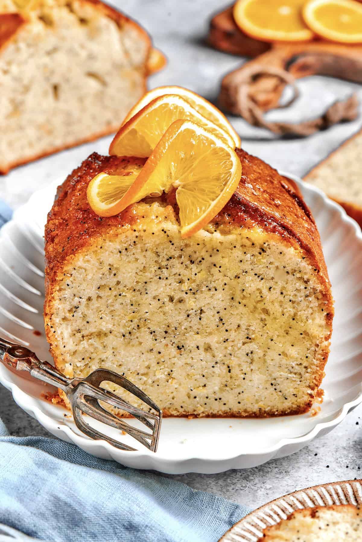 This moist orange poppy seed bread is soaked in a zippy citrus glaze for a bright, tender, bakery-style loaf perfect for brunch or gifting. a loaf of orange poppy seed bread, sliced through the center, with fresh oranges slices on top