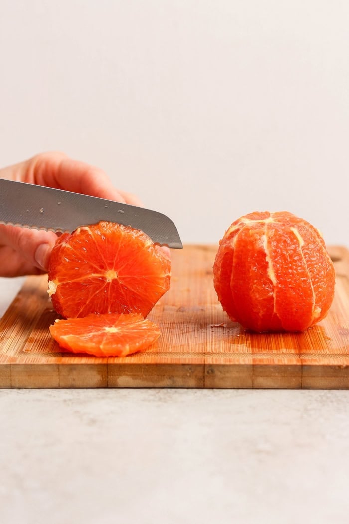 a hand cutting oranges that have the peel cut off, into slices