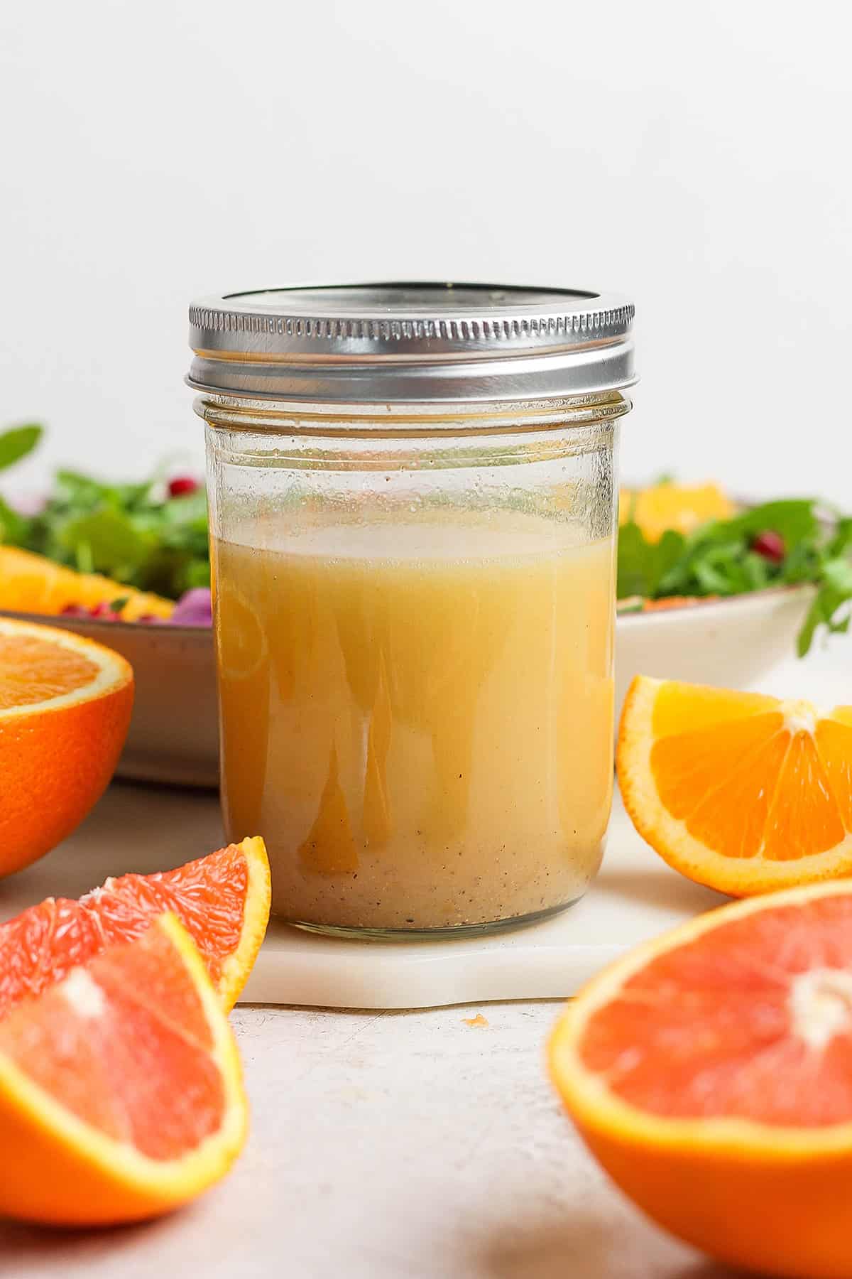 a small jar of citrus vinaigrette salad dressing, with cut fresh citrus and a bowl of salad greens