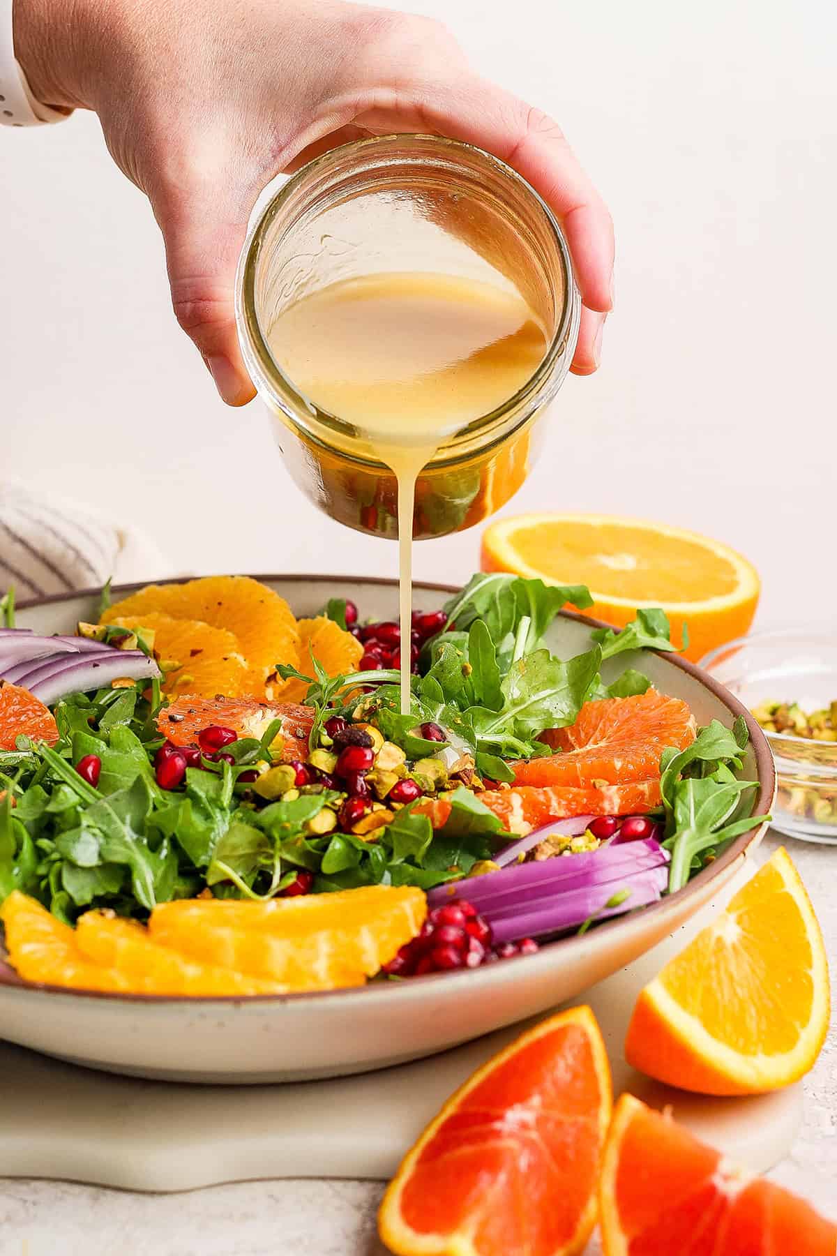 a hand pouring citrus vinaigrette over a bowl of salad greens with fresh citrus slices