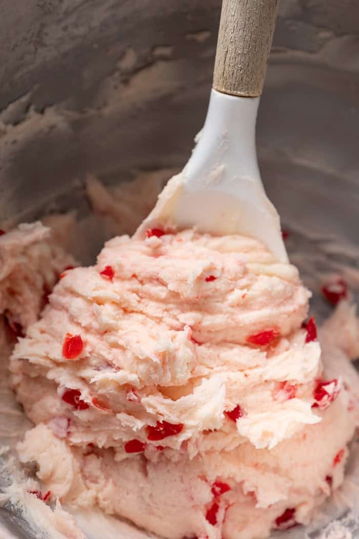 These fudgy cherry brownies are layered with fluffy cherry buttercream and smooth chocolate glaze for an indulgent bakery-style dessert! cherry buttercream frosting in a bowl with a spatula