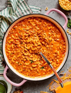 overhead photo of a pink pot of cheesy hamburger helper on a table with cheese and pasta