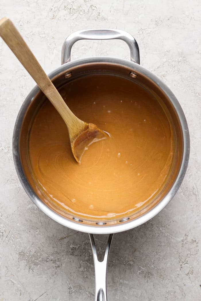 Peanut butter mixture in saucepan with wooden spoon.