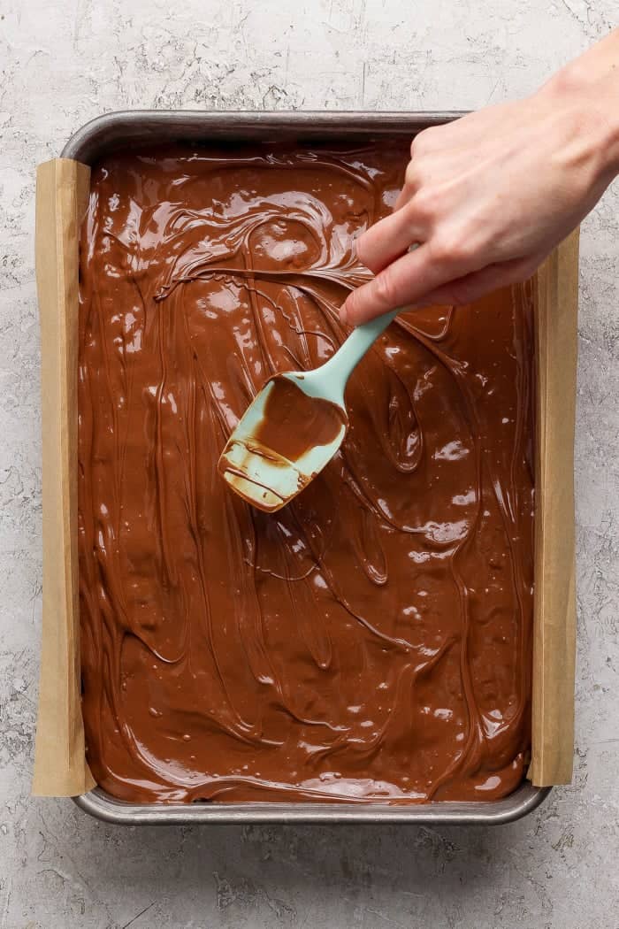 Spreading chocolate layer onto pan of scotcheroos.