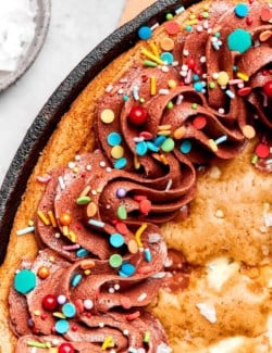 close-up photo of chocolate chip skillet cookie decorated with chocolate frosting and colorful sprinkles