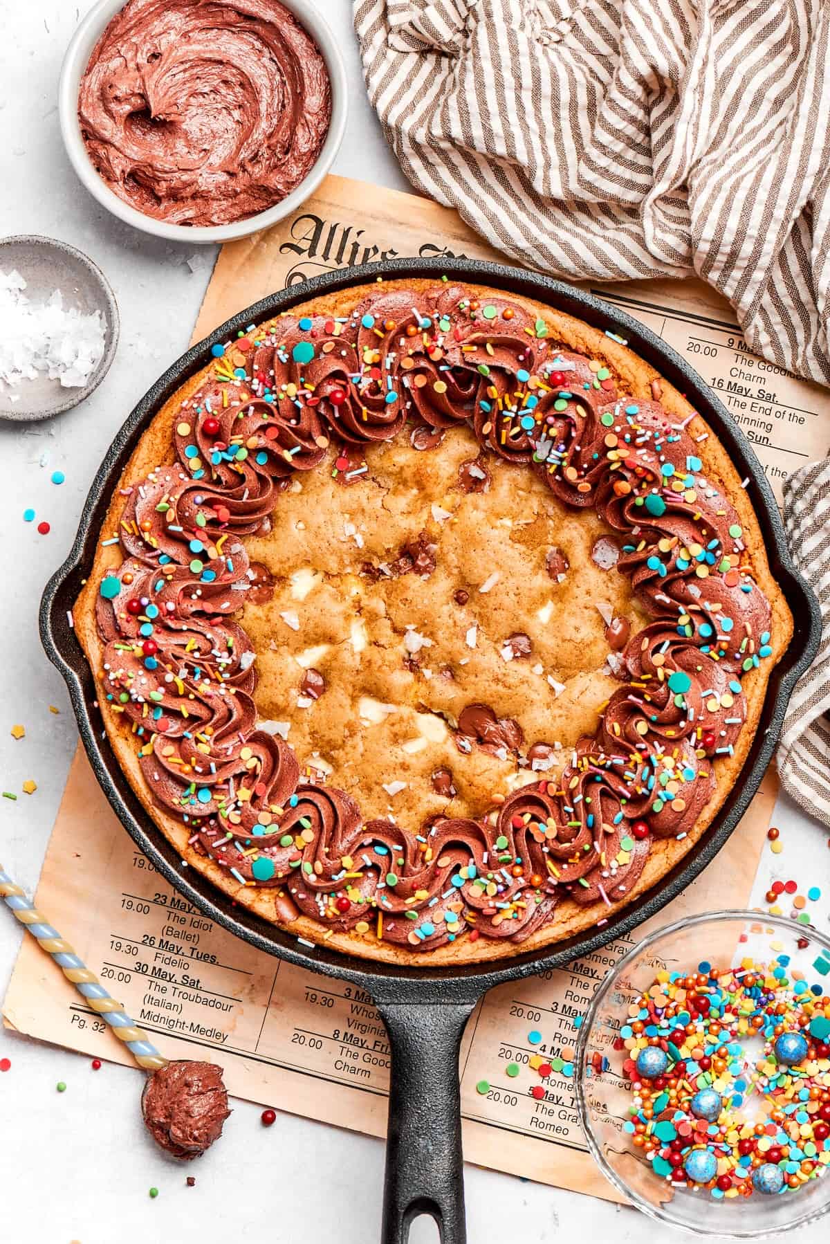 Nutty brown butter, flaky sea salt and fluffy buttercream make this chewy chocolate chip skillet cookie worthy of a celebration. So easy too! overhead photo of chocolate chip skillet cookie decorated with chocolate frosting and colorful sprinkles