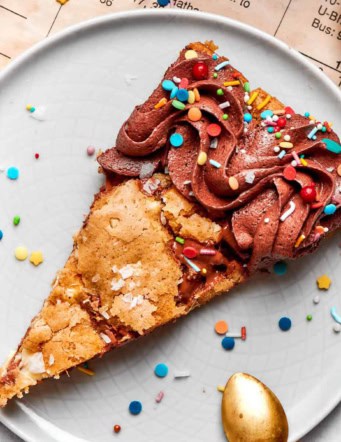 close-up photo of a piece of chocolate chip skillet cookie decorated with chocolate frosting and colorful sprinkles