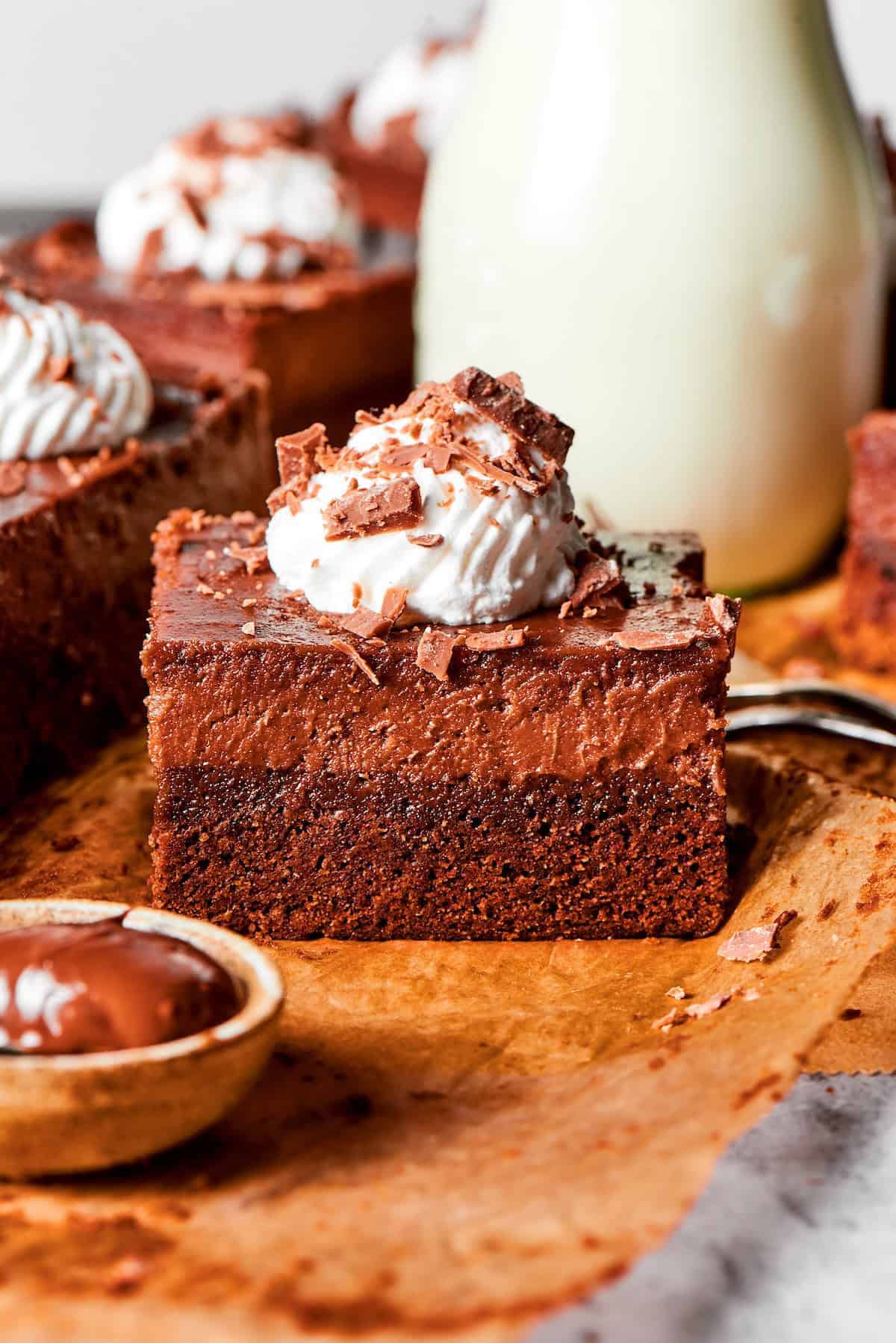 These Nutella cheesecake bars top a fudgy brownie base with creamy Nutella cheesecake for a rich, decadent dessert that’s surprisingly easy! side view of a Nutella cheesecake bar with whipped cream and chocolate shavings on top