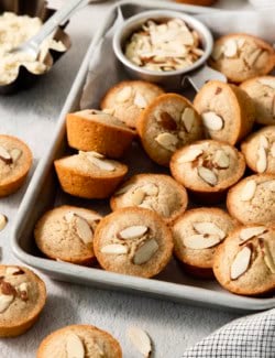 Financiers on sheet pan with bowl of almonds.