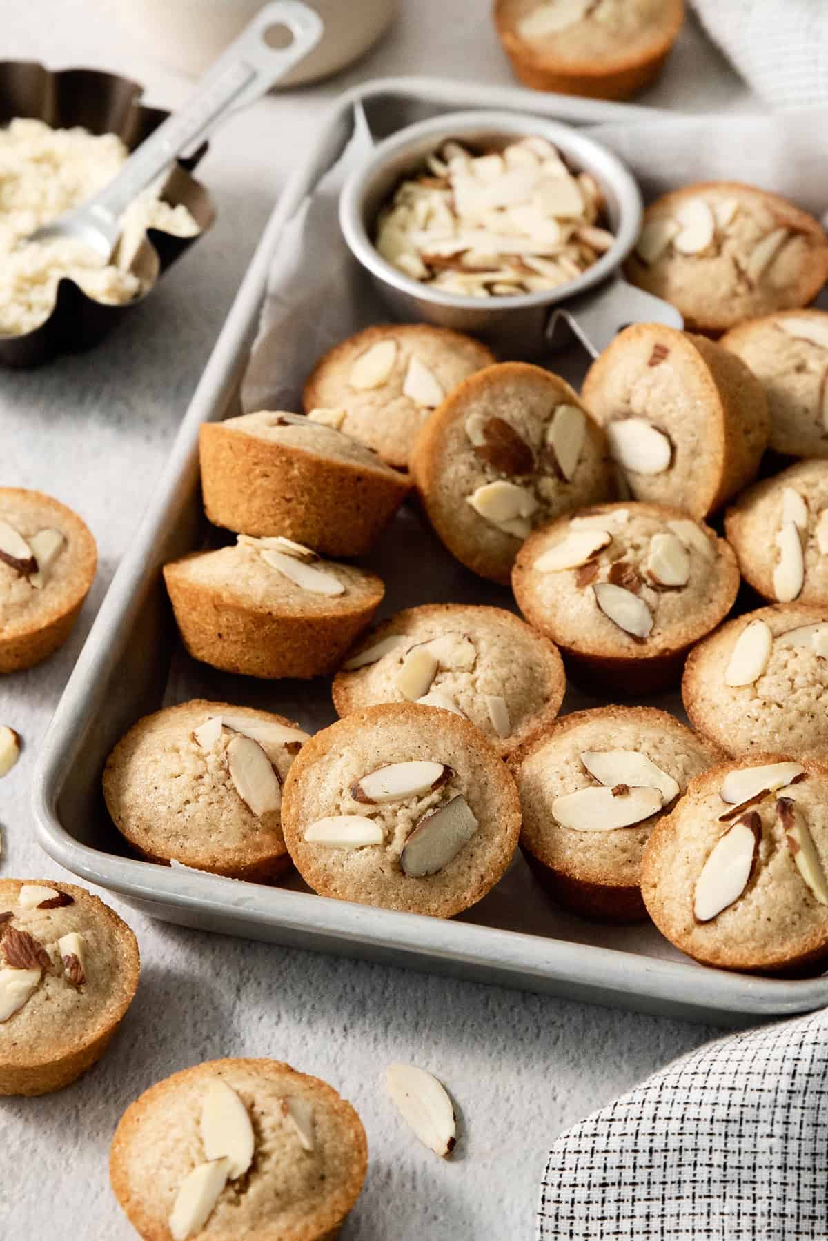 Financiers are an elegant treat that feels straight from a French bakery! My version is made in a muffin pan, so it's easy for home bakers. Financiers on sheet pan with bowl of almonds.