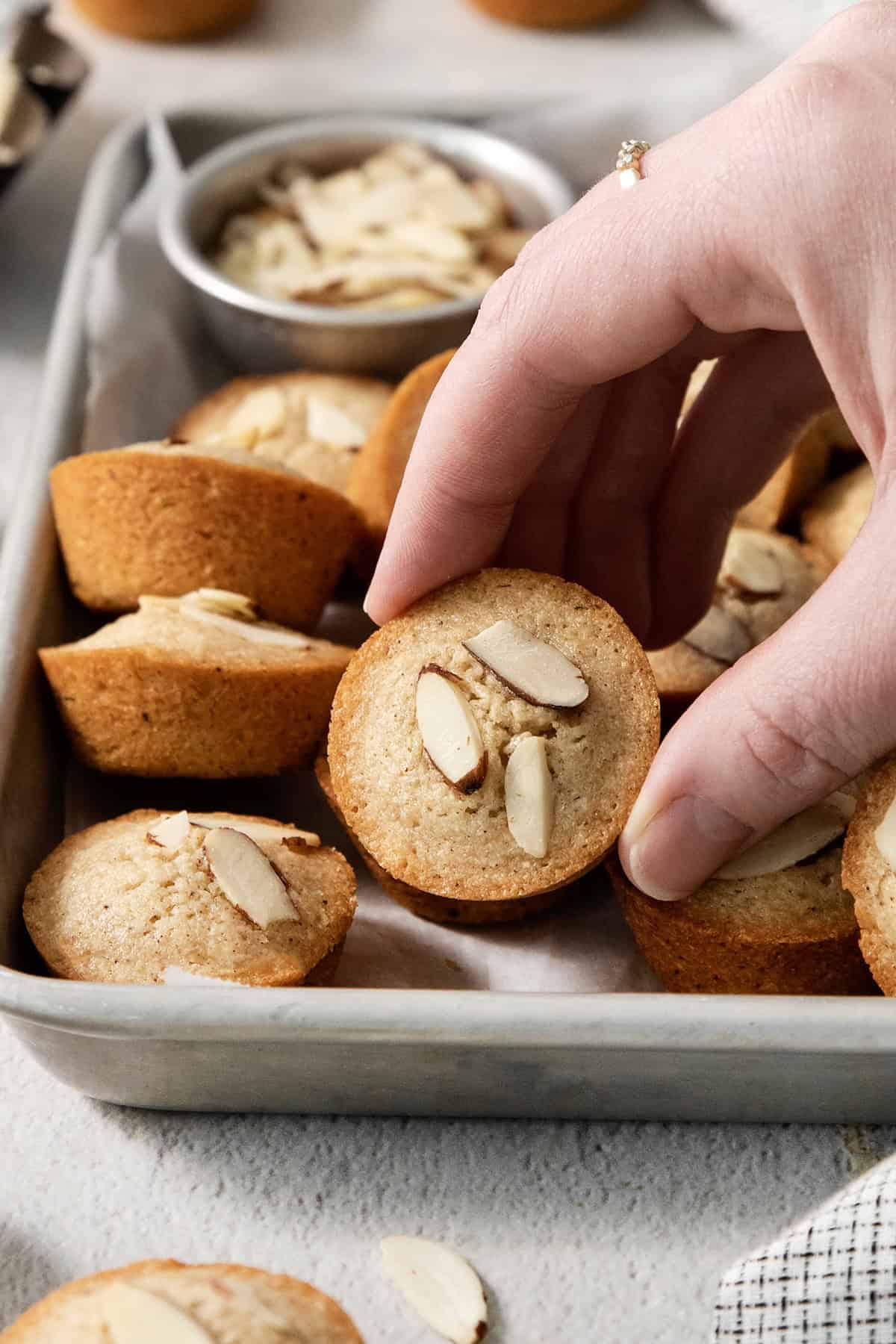 Financiers are an elegant treat that feels straight from a French bakery! My version is made in a muffin pan, so it's easy for home bakers. Hand picking up financiers from pan.