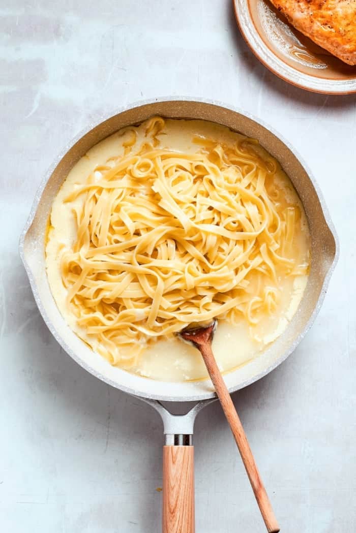 This chicken fettuccine Alfredo pairs chewy pasta with a garlicky Parmesan cream sauce and pan-fried chicken for a restaurant-worthy meal. Stirring fettuccine into skillet of alfredo sauce.