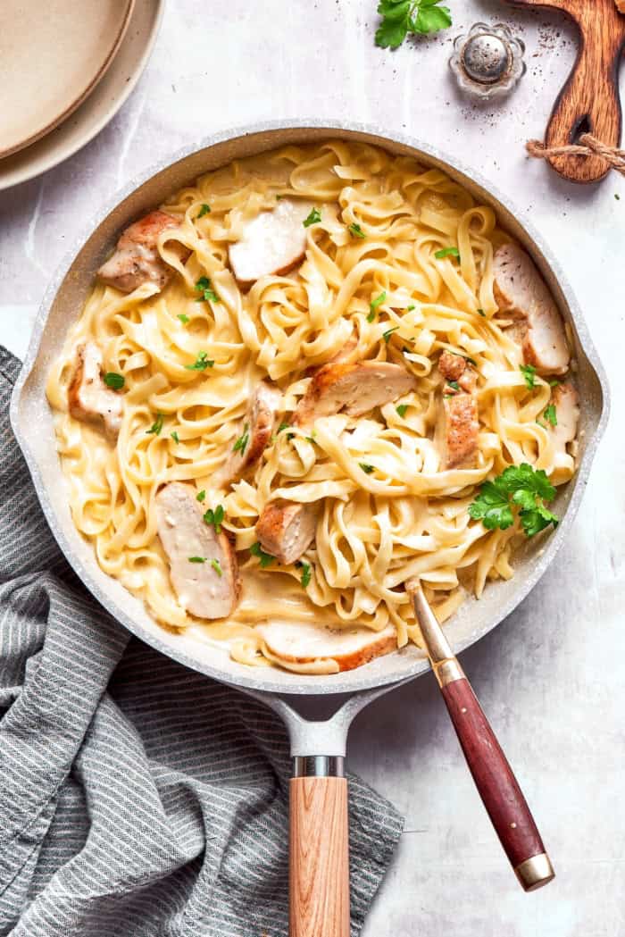 This chicken fettuccine Alfredo pairs chewy pasta with a garlicky Parmesan cream sauce and pan-fried chicken for a restaurant-worthy meal. Chicken fettuccine alfredo in skillet.