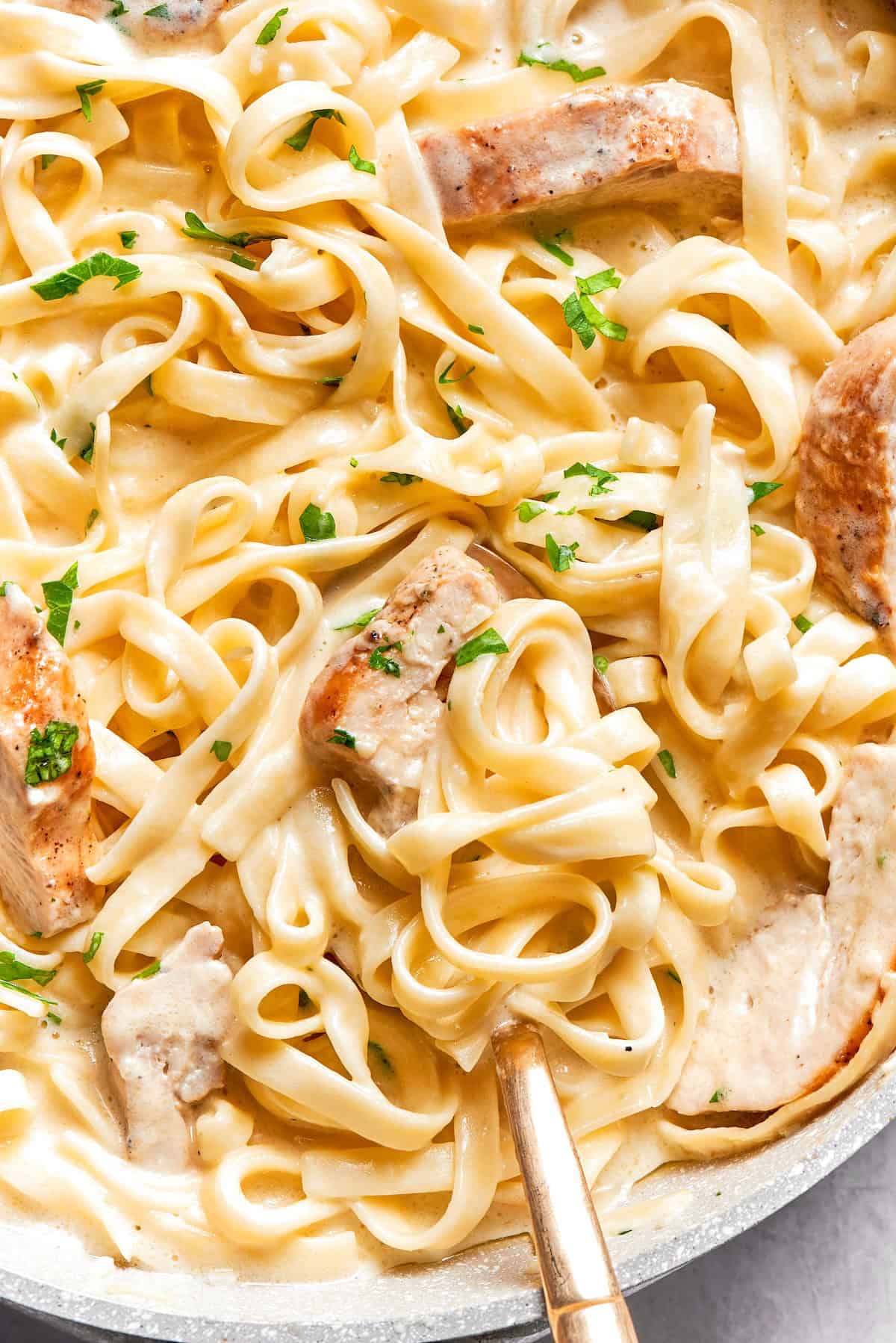 This chicken fettuccine Alfredo pairs chewy pasta with a garlicky Parmesan cream sauce and pan-fried chicken for a restaurant-worthy meal. Skillet of chicken fettuccine alfredo.