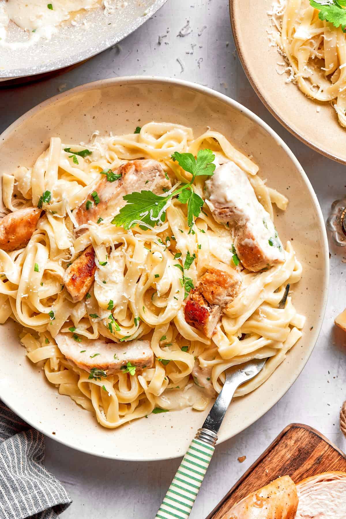 This chicken fettuccine Alfredo pairs chewy pasta with a garlicky Parmesan cream sauce and pan-fried chicken for a restaurant-worthy meal. Chicken fettuccine alfredo in bowl with fork and parsley for garnish.