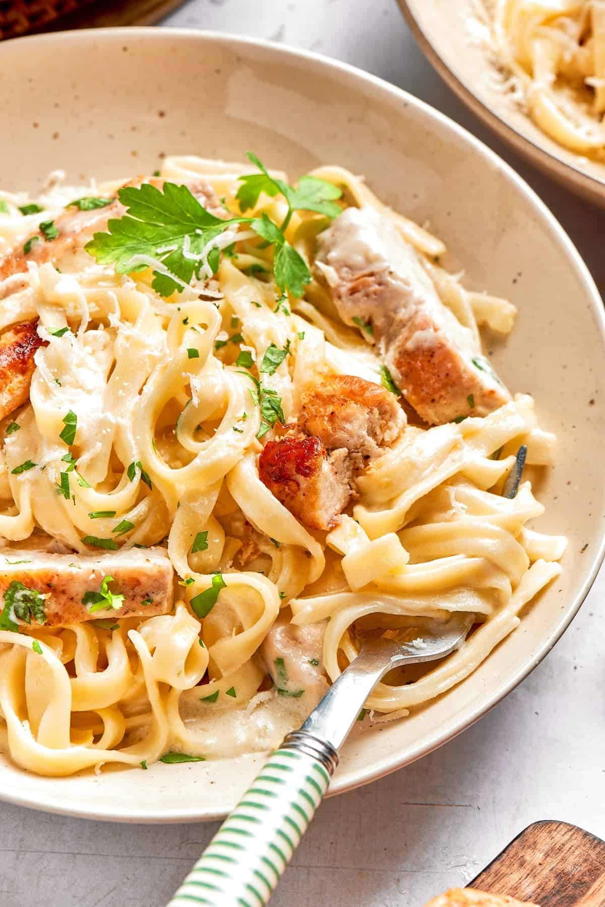 This chicken fettuccine Alfredo pairs chewy pasta with a garlicky Parmesan cream sauce and pan-fried chicken for a restaurant-worthy meal. Bowl of chicken fettuccine alfredo with fork.