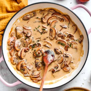 creamy mushroom sauce in a round pink braiser, with a wooden spoon