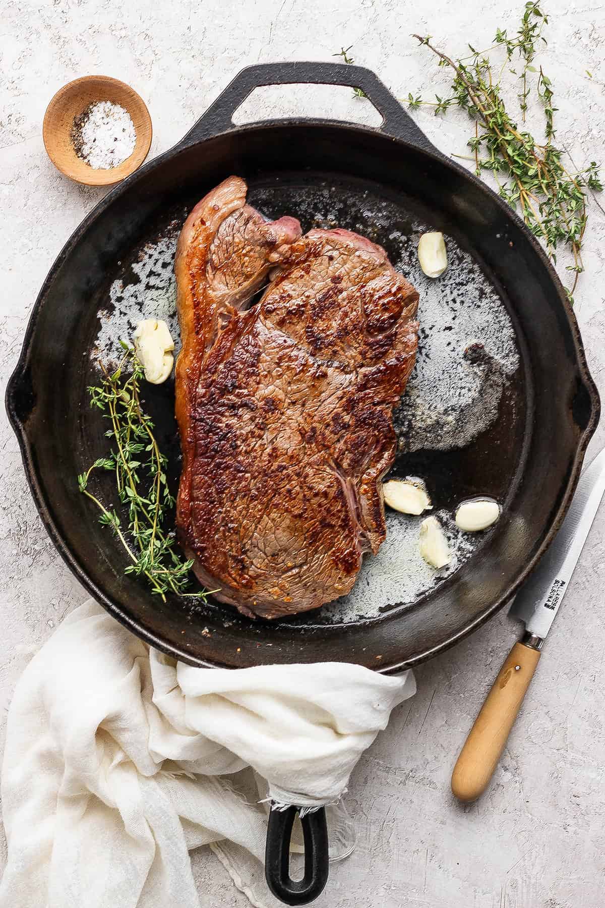 This cast iron skillet steak is tender and perfectly seared, with a rich garlic butter finish. The best way to cook steak on the stovetop! Steak in cast iron skillet with thyme, garlic cloves, and butter.