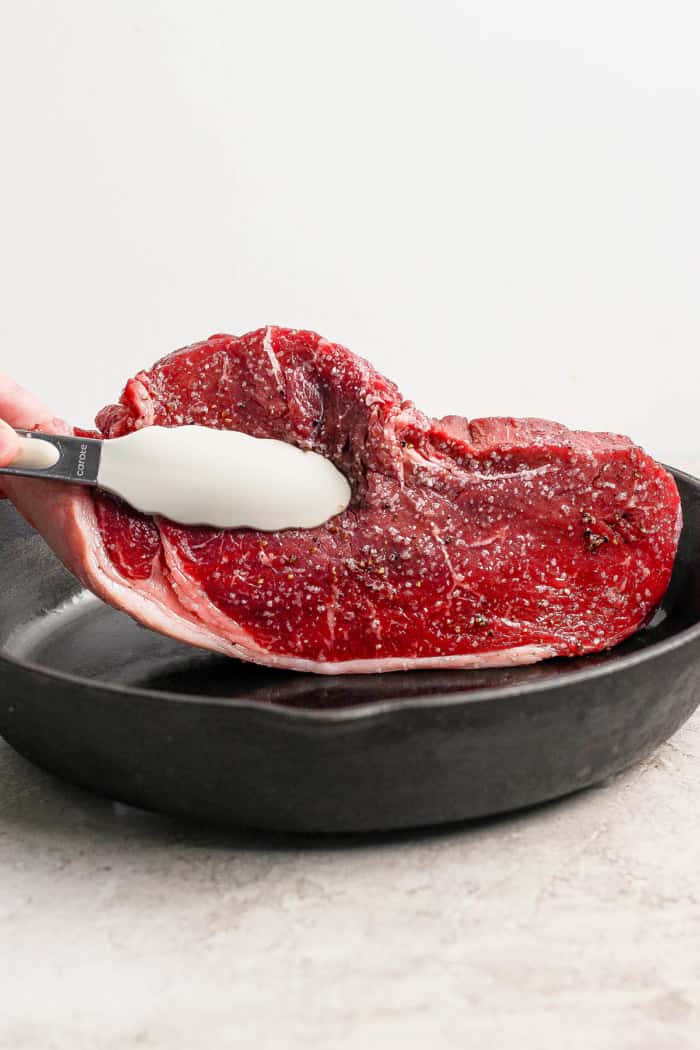 This cast iron skillet steak is tender and perfectly seared, with a rich garlic butter finish. The best way to cook steak on the stovetop! Tongs placing steak into cast iron skillet.