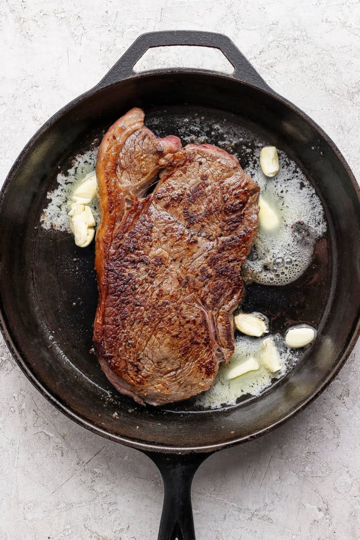 This cast iron skillet steak is tender and perfectly seared, with a rich garlic butter finish. The best way to cook steak on the stovetop! Steak in cast iron skillet with smashed garlic and butter.