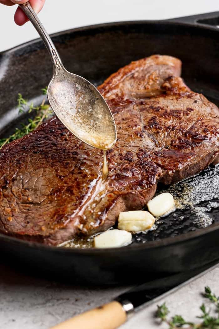 This cast iron skillet steak is tender and perfectly seared, with a rich garlic butter finish. The best way to cook steak on the stovetop! Spooning garlic butter over steak in cast iron skillet.