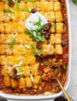 overhead photo of taco tater tot casserole in a white 9 x 13 baking pan, with a portion removed