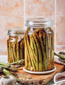 two jars of pickled asparagus on a wood cutting board
