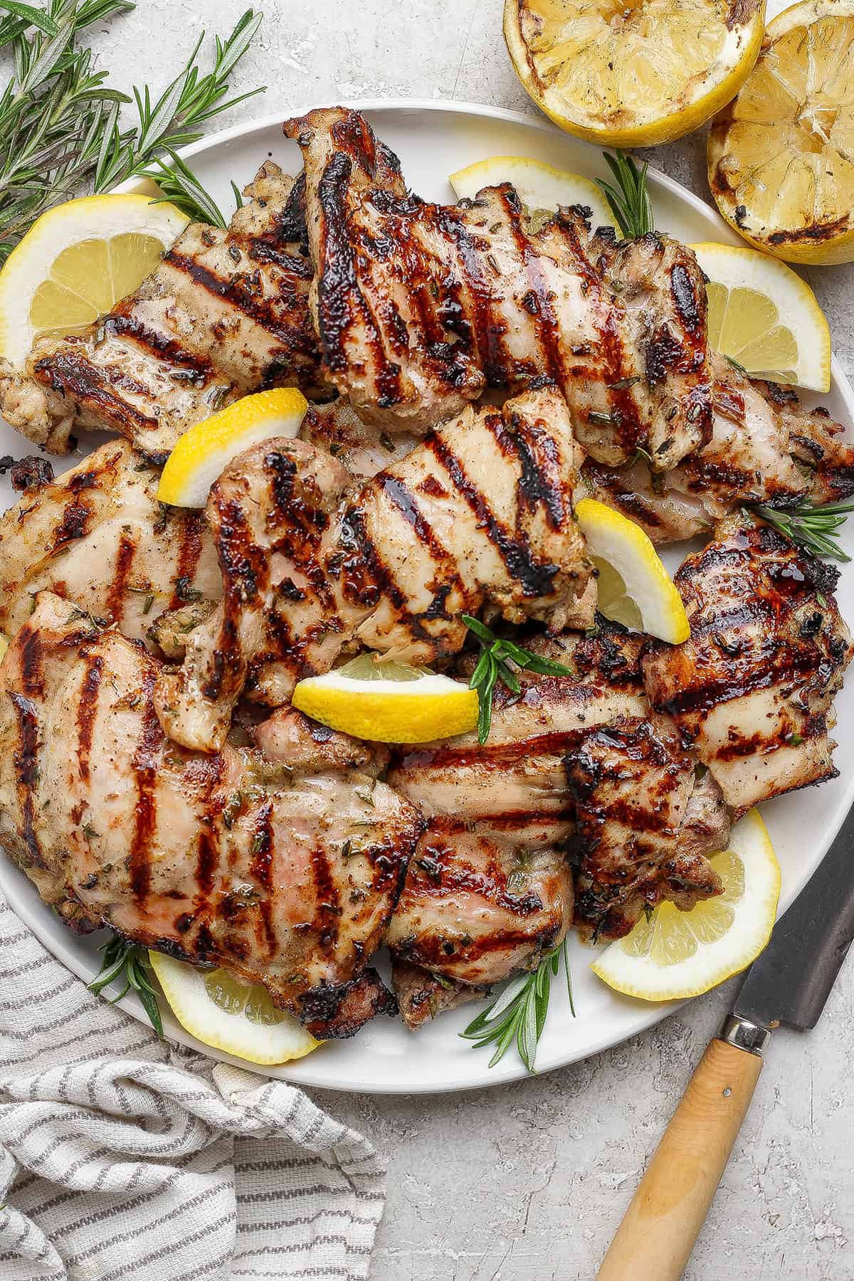 These grilled lemon chicken thighs are juicy and smoky, with a fresh lemon-herb marinade to brighten things up. The perfect summer main dish! Grilled lemon chicken thighs on platter.