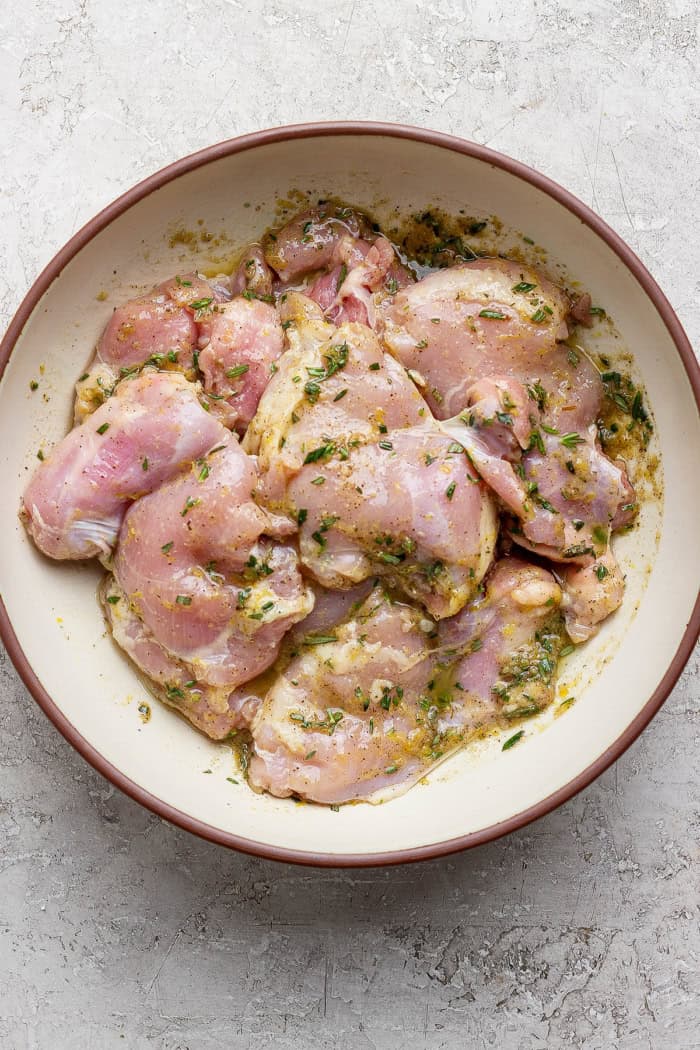 These grilled lemon chicken thighs are juicy and smoky, with a fresh lemon-herb marinade to brighten things up. The perfect summer main dish! Chicken thighs in bowl with lemon herb marinade.