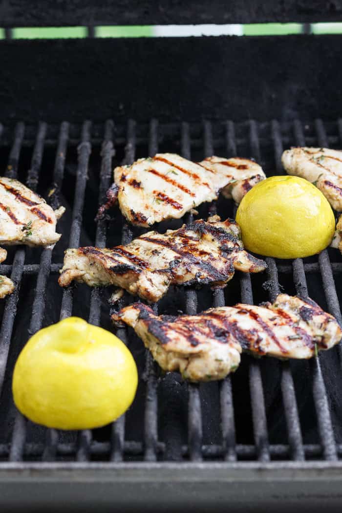 These grilled lemon chicken thighs are juicy and smoky, with a fresh lemon-herb marinade to brighten things up. The perfect summer main dish! Chicken thighs and lemon halves on grill.