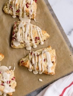 overhead photo of baked rhubarb scones with glaze, on a baking sheet with parchment paper