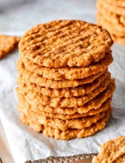 Stack of crispy oat cookies on parchment paper lined pan.