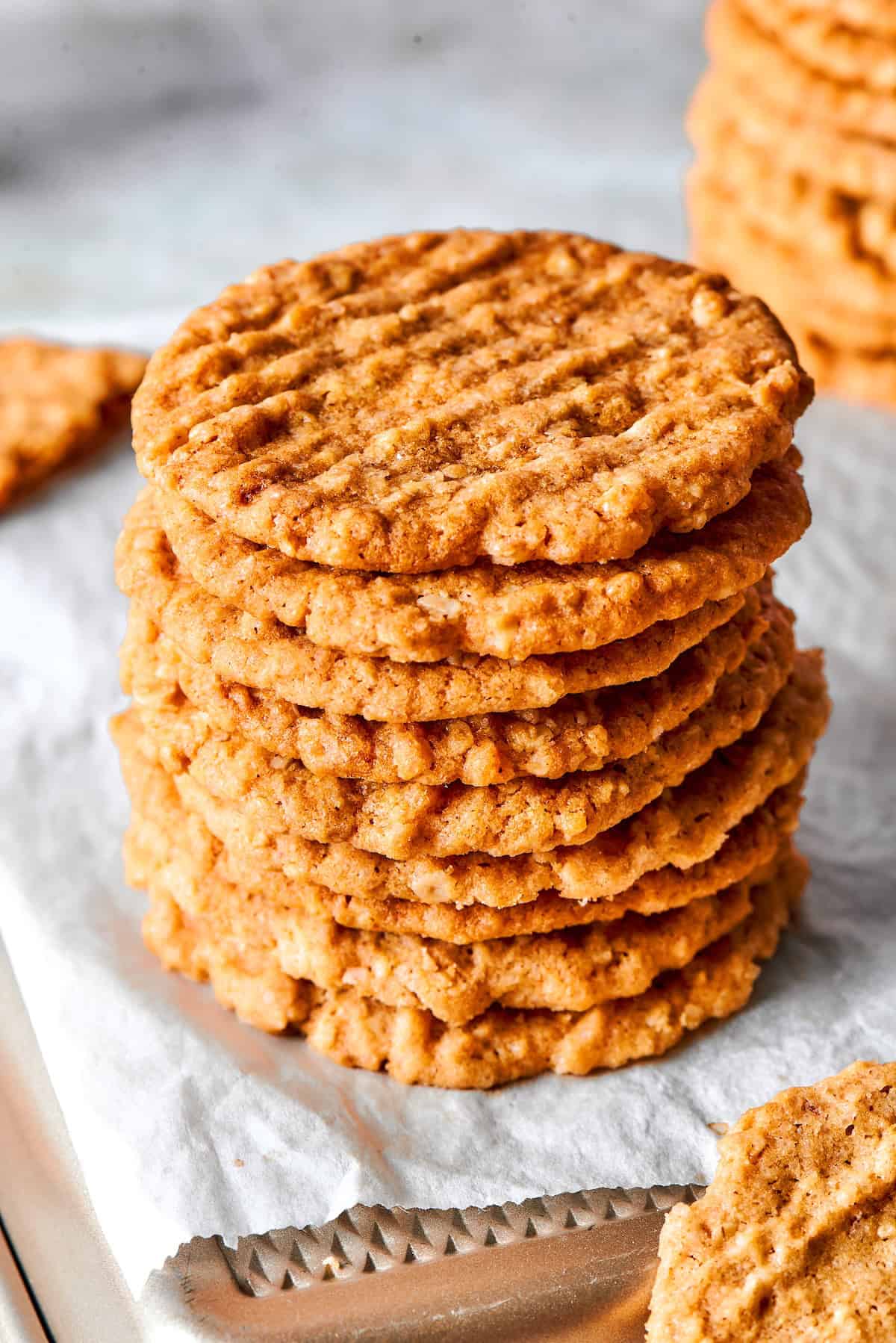 These thin, crispy oat cookies are buttery and golden on the edges, with the most delightful crunch. Made with simple pantry ingredients! Stack of crispy oat cookies on parchment paper lined pan.