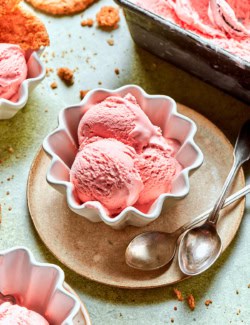 scoops of pink rhubarb ice cream in white fluted bowls, with crispy oat cookies