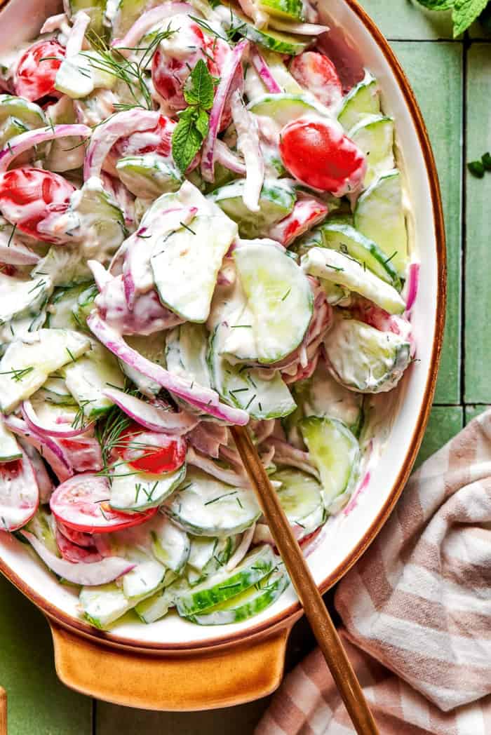 close-up overhead photo of a creamy salad of fresh cucumbers and tomatoes in an oval serving bowl