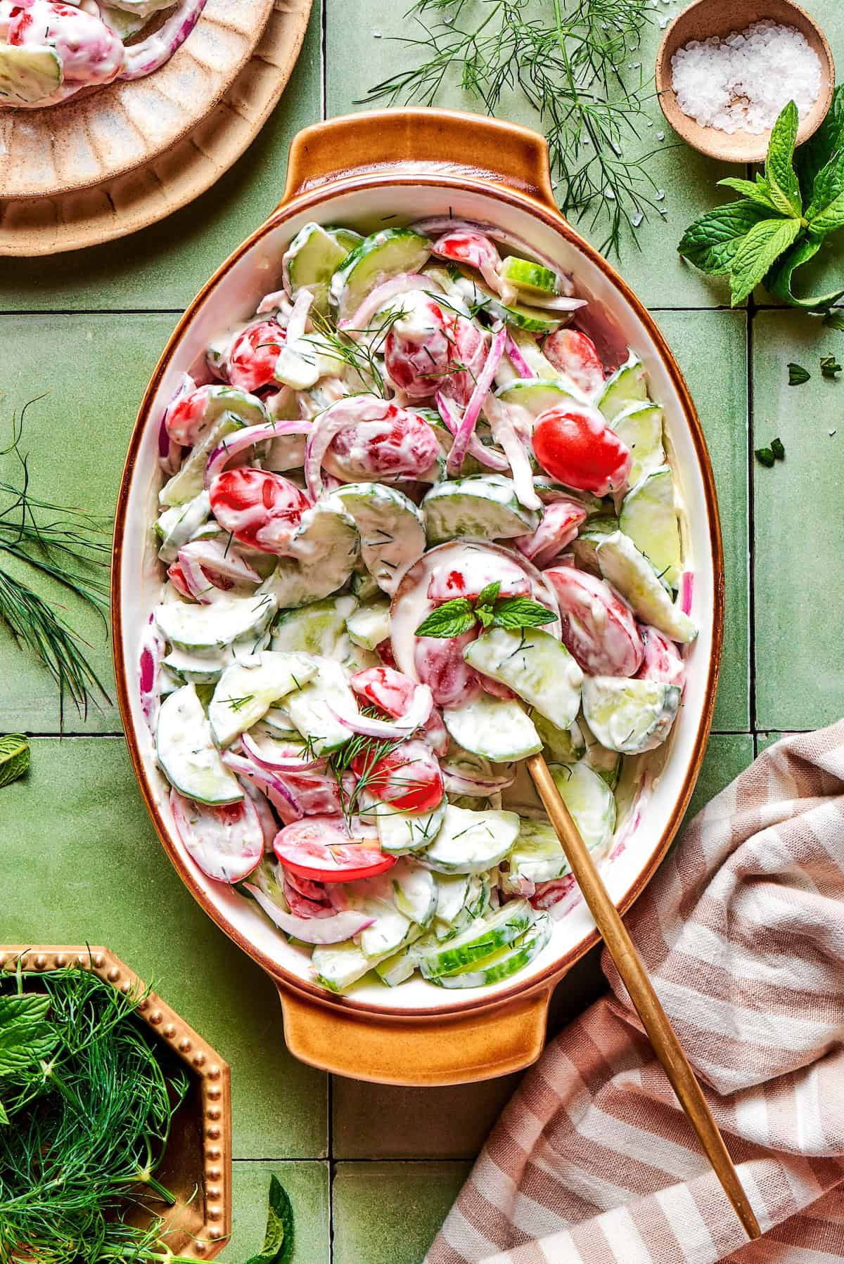 overhead photo of a creamy cucumber and tomato salad in an oval serving bowl